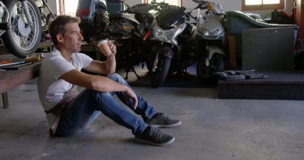 Πλευρική Όψη Του Καυκάσιου Άνδρα Μηχανικός Πίνοντας Καφέ Στο Συνεργείο — Αρχείο Βίντεο