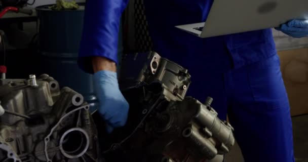 在车库修理摩托车发动机时 使用笔记本电脑的白种男性机械师的前视图 他戴着防护面具 — 图库视频影像