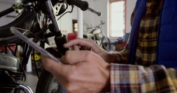 在摩托车修理车库 中使用数字平板电脑的白种男性机械师的侧视图 — 图库视频影像