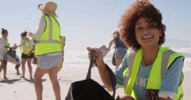 Güneşli bir günde, Afrika kökenli Amerikalı gönüllü bir kadının plajı temizleyişinin ön görüntüsü. Gülümsüyor ve kameraya bakıyor. 