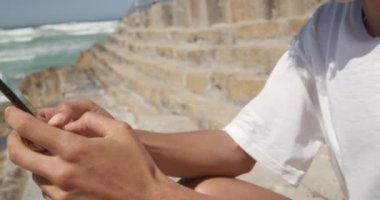 Sahilde cep telefonu kullanan Afrikalı Amerikalı kadının yan görünümü. O 4k gülümsüyor