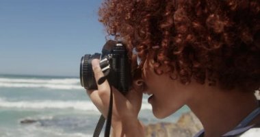 Sahilde dijital kamera ile fotoğraf çeken Afrikalı kadının yan görünümü. O plajda 4k duruyor