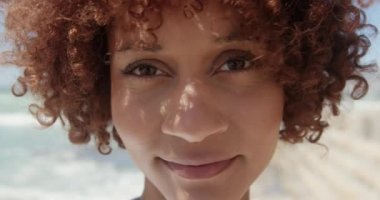 Sahilde kameraya bakan Afrikalı Amerikalı kadının ön görünümü. O gülümsüyor ve kamera 4k bakıyor