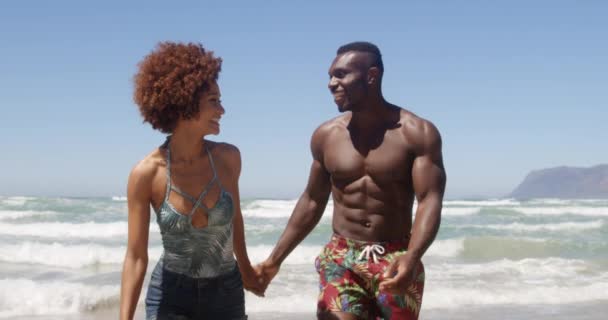 手をつないでビーチで一緒に走っている若いアフリカ系アメリカ人カップルの正面 彼らは微笑んでお互いを見ている — ストック動画