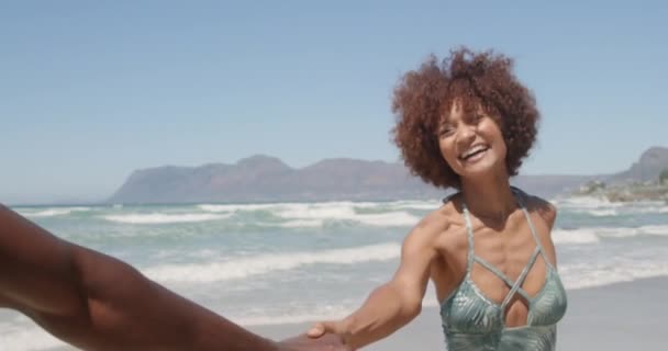 年轻的非洲裔美国妇女手牵手 在阳光下在沙滩上奔跑 她微笑着 玩得很开心 — 图库视频影像