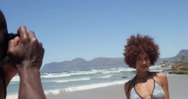Sahilde dijital kamera ile Afrikalı Amerikalı kadının fotoğraflarını çeken genç Afrikalı-Amerikalı adam yan görünümü. O 4k poz