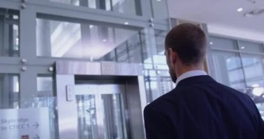 Modern ofisin koridorunda asansör bekleyen beyaz iş adamının dikiz görüntüsü. Düğmeye basıyor. 