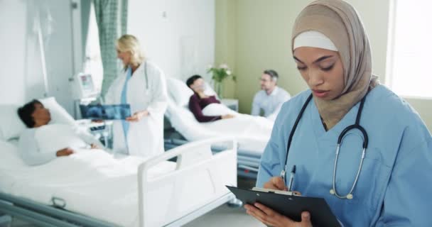 病院病棟でヒジャーブを着用した若い混合人種の女性インターンのフロントビューを閉じます 女性の医者が患者と話しながら彼女はカメラに向かって微笑む — ストック動画