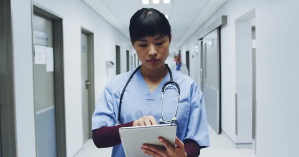 年轻的亚洲女医生用平板电脑站在繁忙的医院走廊前 她抬起头来 微笑着拍照 — 图库视频影像