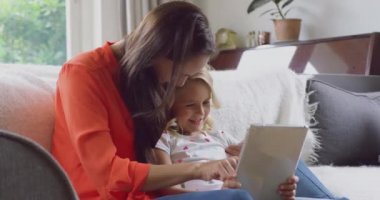 Evde kanepeüzerinde dijital tablet kullanarak Kafkas anne ve kızı ön görünümü. Onlar gülümsüyor ve kanepede 4k birlikte oturuyor