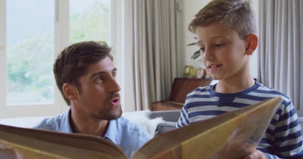 前视图的白种人父亲和儿子在家里读故事书 他们微笑着 互相交流4K — 图库视频影像