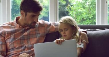 Evde 4k kanepeüzerinde dizüstü bilgisayar kullanarak Kafkas baba ve kızı yan görünümü