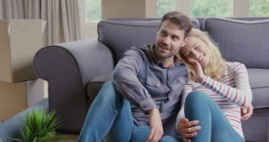 Beyaz bir çiftin evdeki oturma odasında yan yana oturması ön planda.