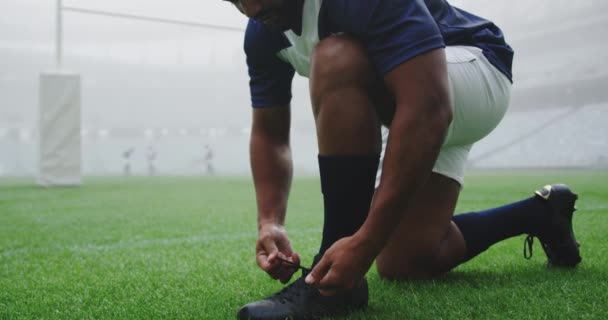 Närbild Afroamerikanska Rugbyspelare Som Knyter Skosnören Arenan Lagkamrater Som Spelar — Stockvideo