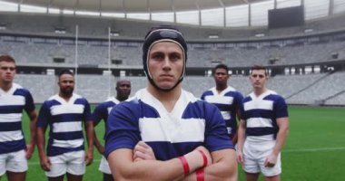 Stadyumda kolları çapraz duran beyaz erkek rugby oyuncusunun ön görüntüsü. 4K kamerasına bakıyor.