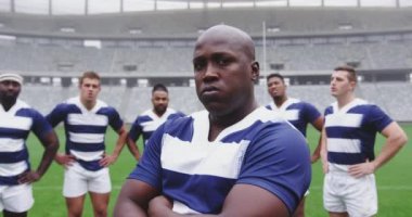 Afrika kökenli Amerikalı erkek rugby oyuncusunun stadyumda kolları çapraz duruşu. 4K kamerasına bakıyor.