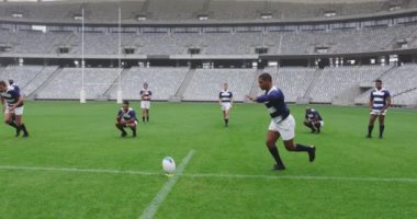 Front view of African American male rugby player kicking rugby ball in ground at stadium. They are smiling and celebrating 4k