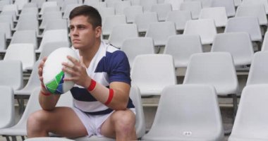 Afrika kökenli Amerikalı erkek rugby oyuncusu stadyumda ragbi topuyla oturuyor. 4k 'ı kaçırıyor.