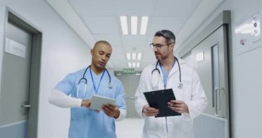 Melez bir ırk ve beyaz bir erkek doktorun hastane koridorunda notları tartışırken belden geriye doğru çekim yapın. 