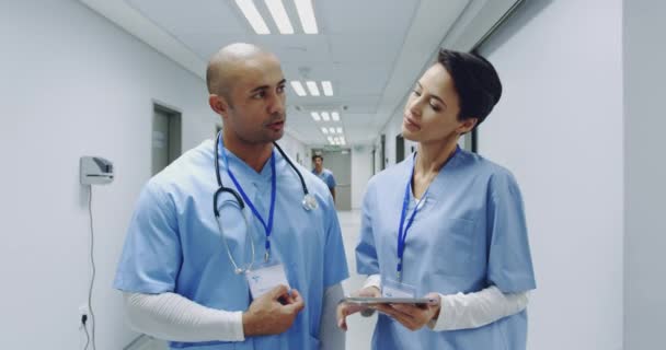 不同种族的男医生和年轻的白人女医生在医院走廊里交谈并握手 医院的工作人员一边说一边走过 — 图库视频影像
