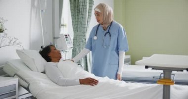 Hasta yatağında yatan, melez ırktan yaşlı bir kadın hastaya tam bir yan bakış açısı. Hajib giyen, melez, genç bir kadın doktor tarafından bakılıyor. 