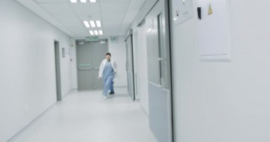 Genç Asyalı kadın doktor ve erkek stajyerlerin acil bir durum için hastane koridorunda koşarken görüntülerini ters çevirin. Koridorun sonundaki kapıdan bakan bir kadın doktor.. 