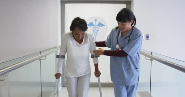 亚洲年轻女医生在医院走廊帮助老年混合种族患者抱着拐杖行走的反向追踪照片 — 图库视频影像
