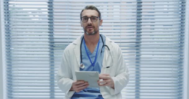 中年白种人男医生在医院使用平板电脑和摄像机对讲机进行锁定拍摄 — 图库视频影像