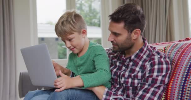 快適な家でラップトップを使用して白人の父と息子の側面図 彼らはソファに座っている — ストック動画