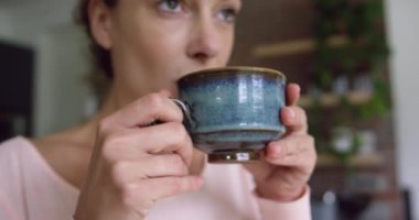 Rahat evde mutfakta kahve içen Beyaz kadının yakın çekim. O gülümsüyor ve uzağa 4k bakıyor