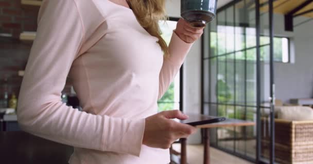 白种妇女喝咖啡和在舒适的家里的厨房使用手机的侧视图 她正在发短信4K — 图库视频影像