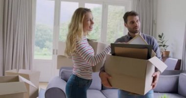 Karton kutular tutan ve yeni evde birbirleriyle etkileşim edebilen Kafkas çiftinin ön görünümü. Kadın gülümseyen ve 4k işaret