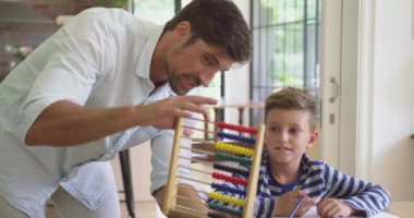 Kafkas baba, rahat bir evde masada oğluna matematik öğretiyor. O abacus 4k kullanıyor