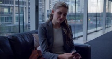 Kafkasyalı iş kadınının lobide koltukta dinlenirken cep telefonuyla konuşması ön planda..