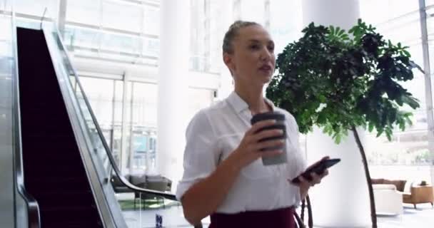 Sidovy Över Kaukasiska Affärskvinna Med Mobiltelefon Och Promenader Lobbyn Kontoret — Stockvideo