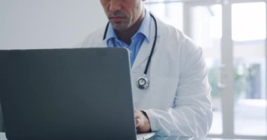 Genç melez erkek doktorun dizüstü bilgisayarla masada oturduğu ön görüntüyü kapat. Ağır çekim. 4k