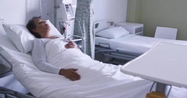 Full length panning shot of senior mixed race woman lying in a hospital bed 