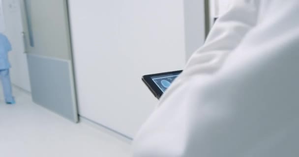 閉じるアップフォローショットの中年白人男性医師歩行で病院の廊下で使用してタブレットコンピュータ — ストック動画