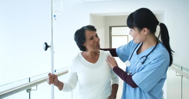 若いですアジアの女性医師のウエストアップビュー暖かく歓迎シニア混合レース女性患者で病院廊下 — ストック動画