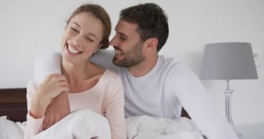 Rahat bir evde yatak odasında yatakta oturan romantik Kafkas çift ön görünümü. Yanak 4k kadın öpüşme Adam