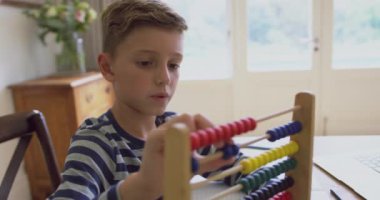 Rahat bir evde masada abaküs üzerinde matematik öğrenen Kafkas çocuğun yakın çekim. O abacus 4k ile oynuyor