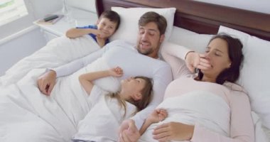 Evde yatak odasında yatakta birlikte dinlenen Kafkas ailesinin yüksek açılı görünümü. Birbirleriyle etkileşime giriyorlar 4k