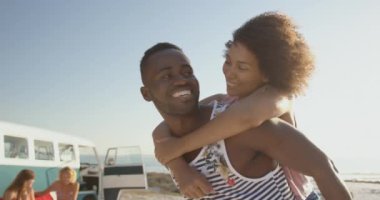 Arkadaşları bir karavanın yanında oturup video izlerken Afro-Amerikan çift kumsalda eğleniyor.