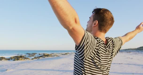 海4Kを眺めながら 腕を組んで浜辺に立つ若い白人男性の側面をクローズアップ — ストック動画