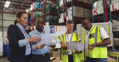 Çeşitli depo çalışanlarından oluşan bir grubun ön görüntüsü. Belgeleri ellerinde tutuyorlar ve birlikte konuşuyorlar. Deponun yükleme bölümünde duruyorlar.