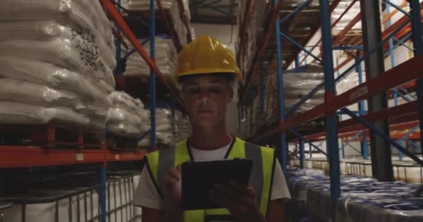 Vue rapprochée de face d'une femme d'âge moyen d'un entrepôt caucasien portant un casque jaune et utilisant une tablette pendant qu'elle patrouille dans les couloirs d'un entrepôt la nuit .