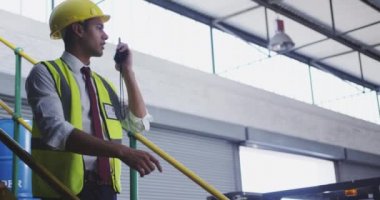 Genç bir Asyalı erkek depo müdürünün bir depodaki basamaklarda dikilip iki yönlü telsizle konuşmasını kapatın.