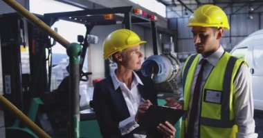 Orta yaşlı beyaz bir kadın depo yöneticisi ve bir depo yükleme koyunda konuşan genç bir Asyalı erkek depo yöneticisi nin ön görünümüne yakın. 4k