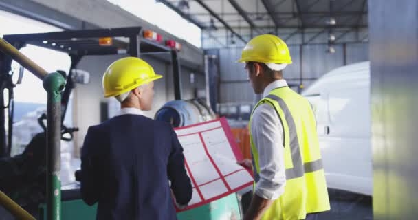 Vue arrière rapprochée d'une femme d'affaires caucasienne d'âge moyen et d'un jeune gérant d'entrepôt asiatique parlant dans un entrepôt et regardant un grand plan qu'elle tient. 4k 
