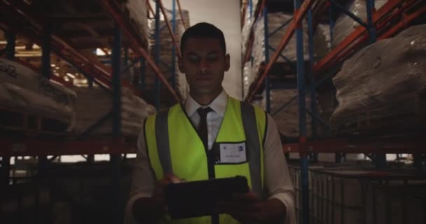 彼は夜に倉庫の廊下をパトロールしながら タブレットコンピュータを使用して若いアジアの男性倉庫労働者のフロントビューを閉じます — ストック動画